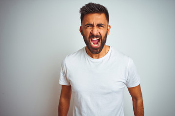 Young indian man wearing t-shirt standing over isolated white background angry and mad screaming...