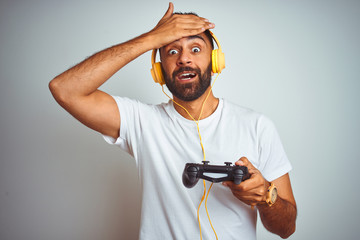 Arab indian gamer man playing video game using headphones over isolated white background stressed with hand on head, shocked with shame and surprise face, angry and frustrated. Fear and upset 