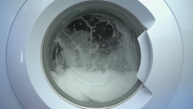 Close up view porthole of washing machine. Washing clothes process in slow motion.