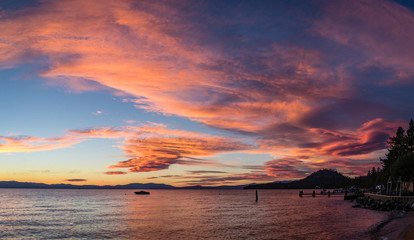 Panorama of a bright pink, orange and blue sunset with a boat in the middle and a dock on the right corner standing on Lakeside Beach at Lake Tahoe