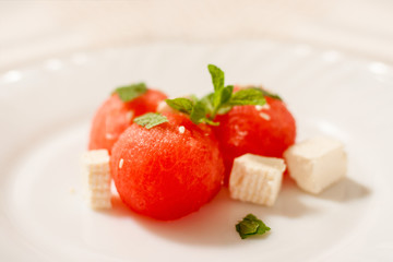 Salad of watermelon balls, feta cheese and mint, sprinkled with sesame seeds in a white plate. Close up