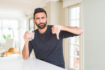 Handsome hispanic man drinking a fresh glass of water with angry face, negative sign showing...