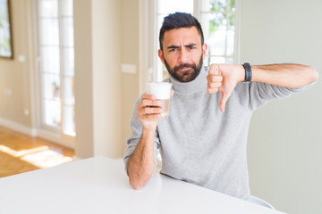 Handsome hispanic man drinking a cup of coffee with angry face, negative sign showing dislike with...