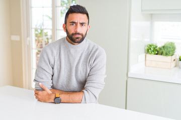 Handsome hispanic man wearing casual sweater at home skeptic and nervous, disapproving expression on face with crossed arms. Negative person.