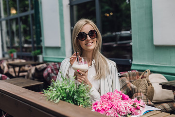 Stylish woman in sunglasses sitting in a summer cafe in the hands of a cocktail glass