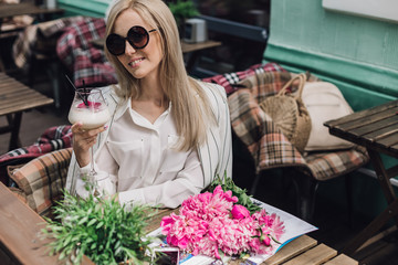 Stylish woman in sunglasses sitting in a summer cafe in the hands of a cocktail glass