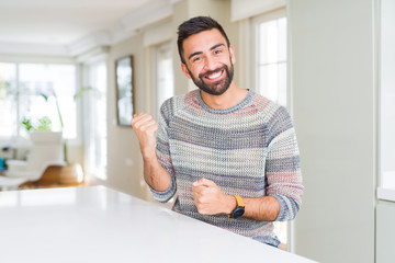 Fototapeta premium Handsome hispanic man wearing casual sweater at home very happy and excited doing winner gesture with arms raised, smiling and screaming for success. Celebration concept.