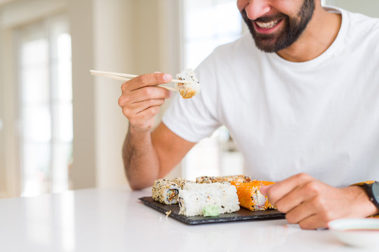 Handsome man smiling happy enjoying eating fresh colorful asian sushi using chopsticks
