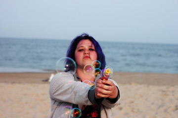 Beautiful woman shooting bubble gun towards the viewer on the beach 