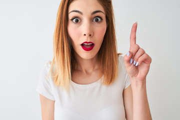 Beautiful redhead woman wearing casual t-shirt standing over isolated white background surprised with an idea or question pointing finger with happy face, number one