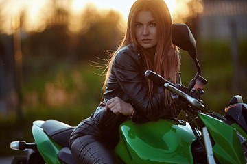 Fototapeta na wymiar Beautiful young girl with a fashionable hairstyle and red lips poses next to motorcycle
