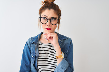 Redhead woman wearing denim shirt and glasses standing over isolated white background serious face...