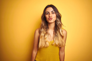 Obraz premium Young beautiful woman wearing t-shirt over yellow isolated background looking at the camera blowing a kiss on air being lovely and sexy. Love expression.