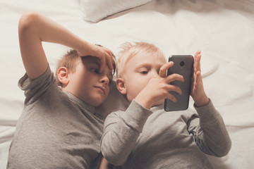 Two boys are lying in bed with a smartphone. Gadget Leisure