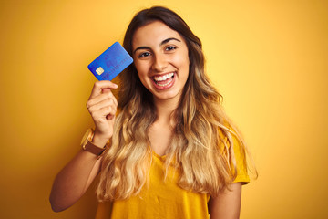 Young beautiful woman holding credit card over yellow isolated background with a happy face...