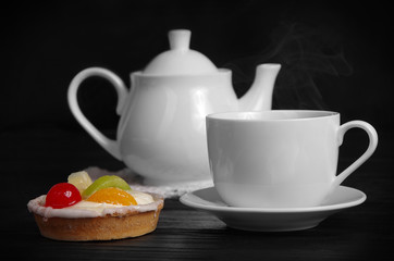 cup of hot tea with cake and teapot on the table