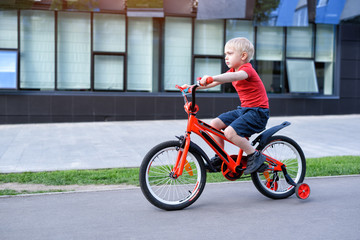 Handsome blond boy rides on a children's bicycle. Urban background