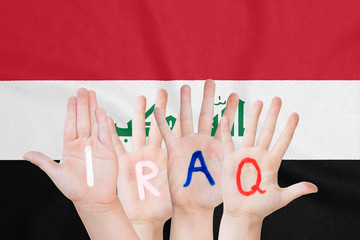Inscription Iraq on the children's hands against the background of a waving flag of the Iraq