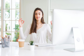 Beautiful young woman working using computer relax and smiling with eyes closed doing meditation gesture with fingers. Yoga concept.