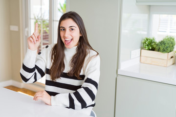 Beautiful young woman wearing stripes sweater pointing finger up with successful idea. Exited and happy. Number one.