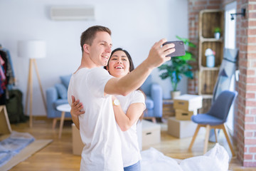 Young beautiful couple standing using smartphone to take a selfie at new home around cardboard boxes