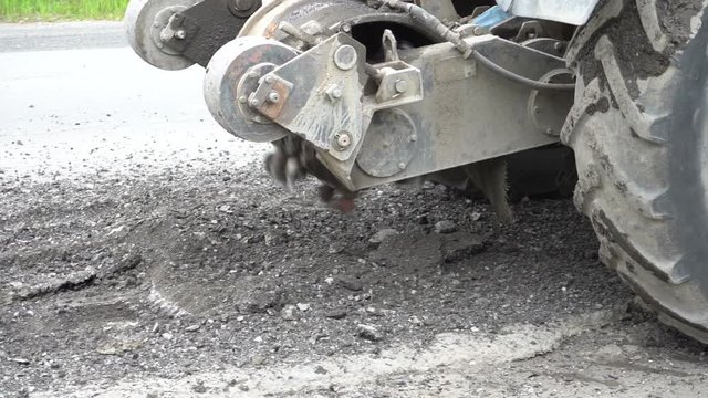 Road milling machine cuts the old asphalt. Road repair. Destruction of the road surface. The cutter cuts a layer of asphalt. Pieces of stone fly apart. Close-up