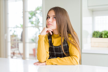 Young beautiful blonde kid girl wearing casual yellow sweater at home with hand on chin thinking about question, pensive expression. Smiling with thoughtful face. Doubt concept.