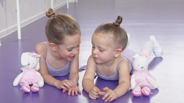 Two little ballerinas lying on the floor at ballet school resting after practicing. Adorable little sisters talking, relaxing after exercising at ballet school. Friendship, childhood, family concept
