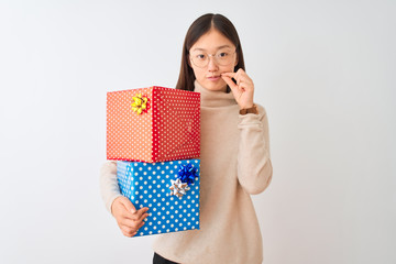 Young chinese woman holding birthday gifts over isolated white background mouth and lips shut as...