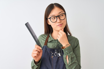 Chinese hairdresser woman wearing glasses holding comb over isolated white background serious face...