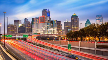 Dallas skyline at dusk. Rush hour traffic leaves light trails on I-75 highway.