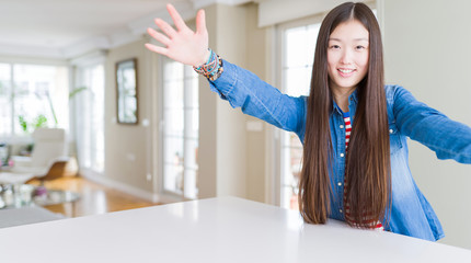 Fototapeta na wymiar Young beautiful asian woman with long hair wearing denim jacket looking at the camera smiling with open arms for hug. Cheerful expression embracing happiness.