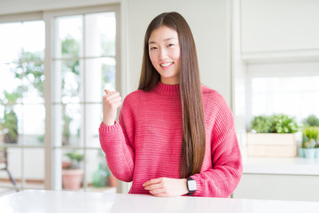 Beautiful Asian woman wearing pink sweater on white table smiling with happy face looking and pointing to the side with thumb up.
