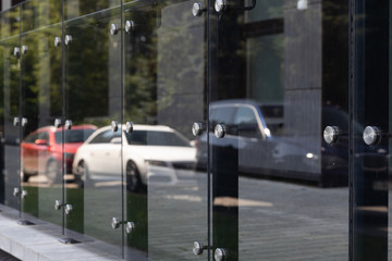 Diagonal view of glass windows or wall with round steel elements with cars and trees reflection on it.