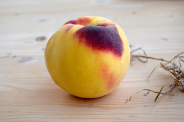 The peach is on a wooden table. Fruit is large, yellow, round, fresh, ripened.