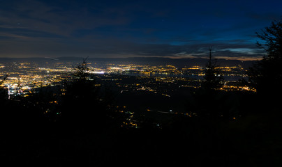 Fototapeta premium Evening top view of city lights, French Annemasse, Swiss Geneva,lake Geneva and picturesque sky with dark clouds after sunset,photo with long exposure.Department of Haute-Savoie in France.