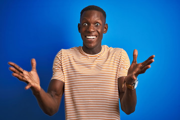 African american man wearing striped casual t-shirt standing over isolated blue background celebrating crazy and amazed for success with arms raised and open eyes screaming excited. Winner concept