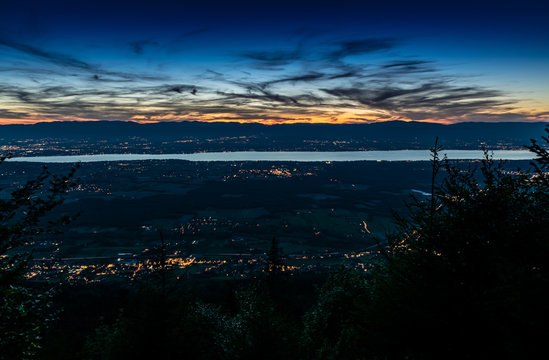 Evening top view of the city lights on Lake Geneva and the blue orange sky with dark clouds after sunset,photo with long exposure.Department of Haute-Savoie in France.