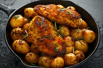 Freshly cooked breaded chicken Kiev's served with crispy baked rosemary potato in rustic cast iron skillet, pan