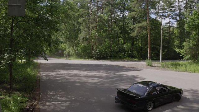 Black car drifting on road turn in countryside front aerial view. Racing car driving with driftage on asphalt. Old car turning with drift. Japanese rear wheel drive car