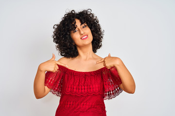Young arab woman with curly hair wearing red dress standing over isolated white background looking...