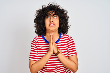 Young arab woman with curly hair wearing striped t-shirt over isolated white background begging and...