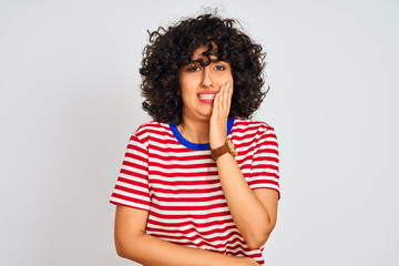 Young arab woman with curly hair wearing striped t-shirt over isolated white background touching mouth with hand with painful expression because of toothache or dental illness on teeth. 