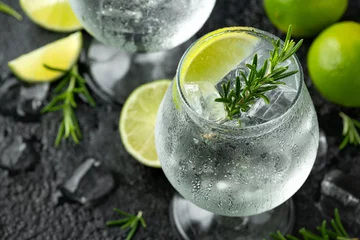 Foto op Plexiglas Gin and Tonic Alcohol drink with Lime, Rosemary and ice on rustic black table © grinchh