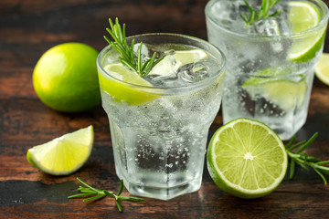 Gin and Tonic Alcohol drink with Lime, Rosemary and ice on wooden table
