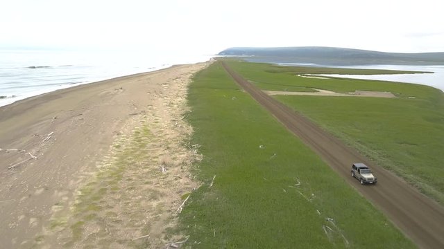 Aerial front view of SUV Jeep driving a coastal dirt road. Nome - Council Highway, Alaska.