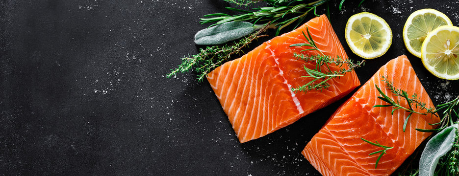 Salmon. Fresh raw salmon fish fillet with cooking ingredients, herbs and lemon on black background, top view, banner