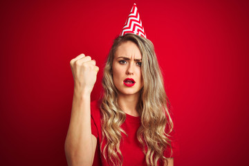 Young beautiful woman wearing bitrhday hat over red isolated background annoyed and frustrated shouting with anger, crazy and yelling with raised hand, anger concept