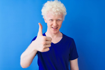 Young albino blond man wearing casual t-shirt standing over isolated blue background doing happy...