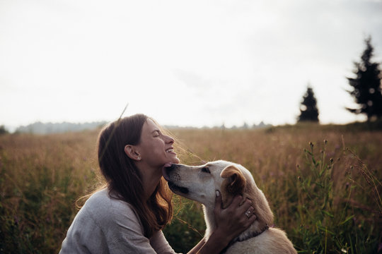 Beautiful young woman relaxed and carefree enjoying a summer sunset with her lovely dog on the straw field background